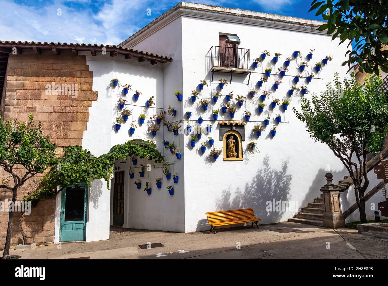 Andalusian neighborhood with blue flower pots hanging on the white walls of Arcos de la frontera, in Poble Espanyol, Spanish Village in Barcelona, Cat Stock Photo