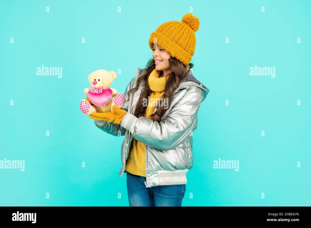 happy child in hat and puffer jacket with toy on blue background, childhood Stock Photo