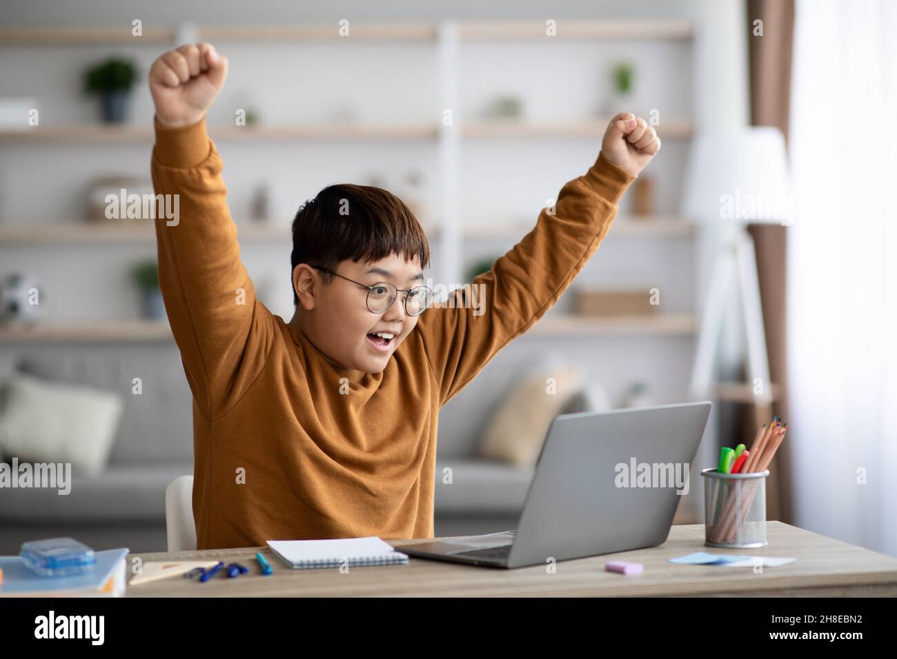 Emotional chubby asian schooler celebrating success, using notebook Stock Photo