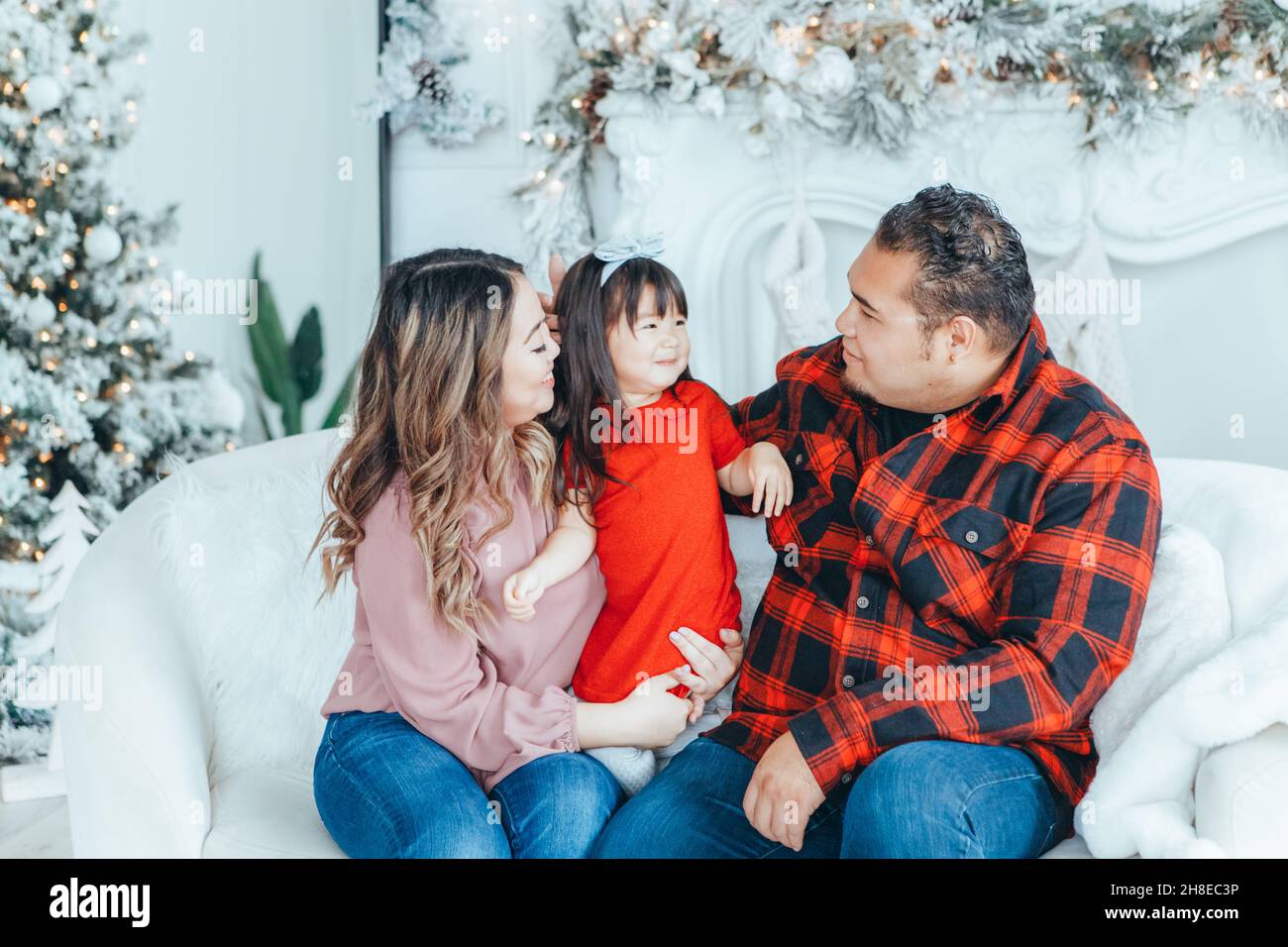 Asian family father, mother with daughter toddler girl celebrating Christmas or New Year. Mixed race mom, dad, daughter by decorating Christas tree at Stock Photo