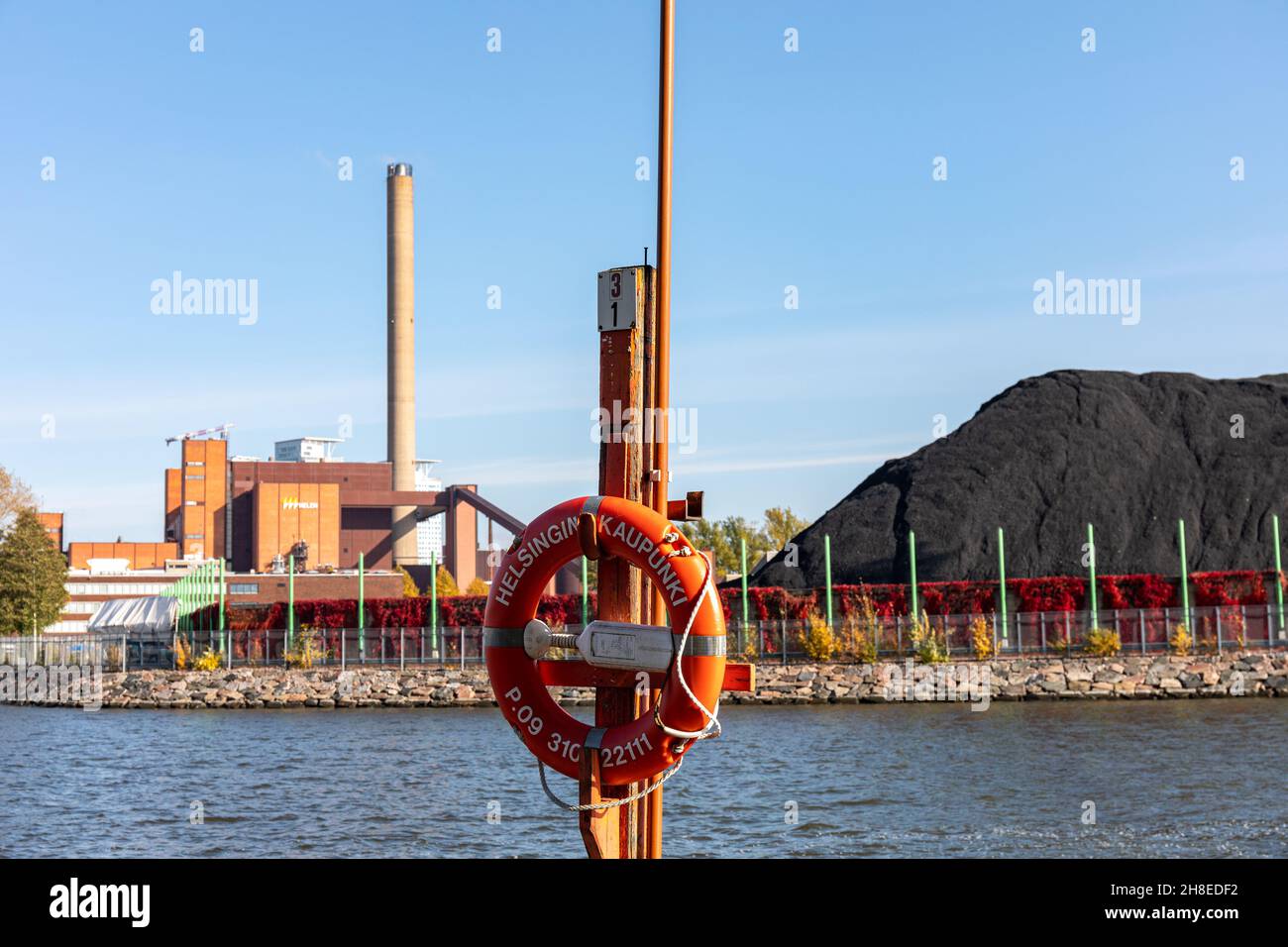 Life buoy in the foreground, Hanasaari Power Plant and coal stock in the background in Merihaka district of Helsinki, Finland Stock Photo