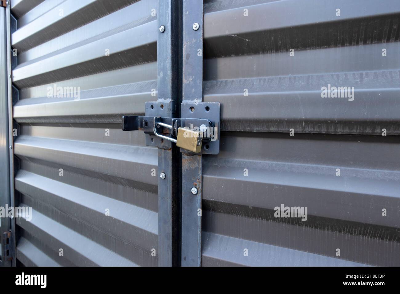 Angled view of a yellow padlock keeping two large metal doors locked up tight in an outdoor storage facility Stock Photo