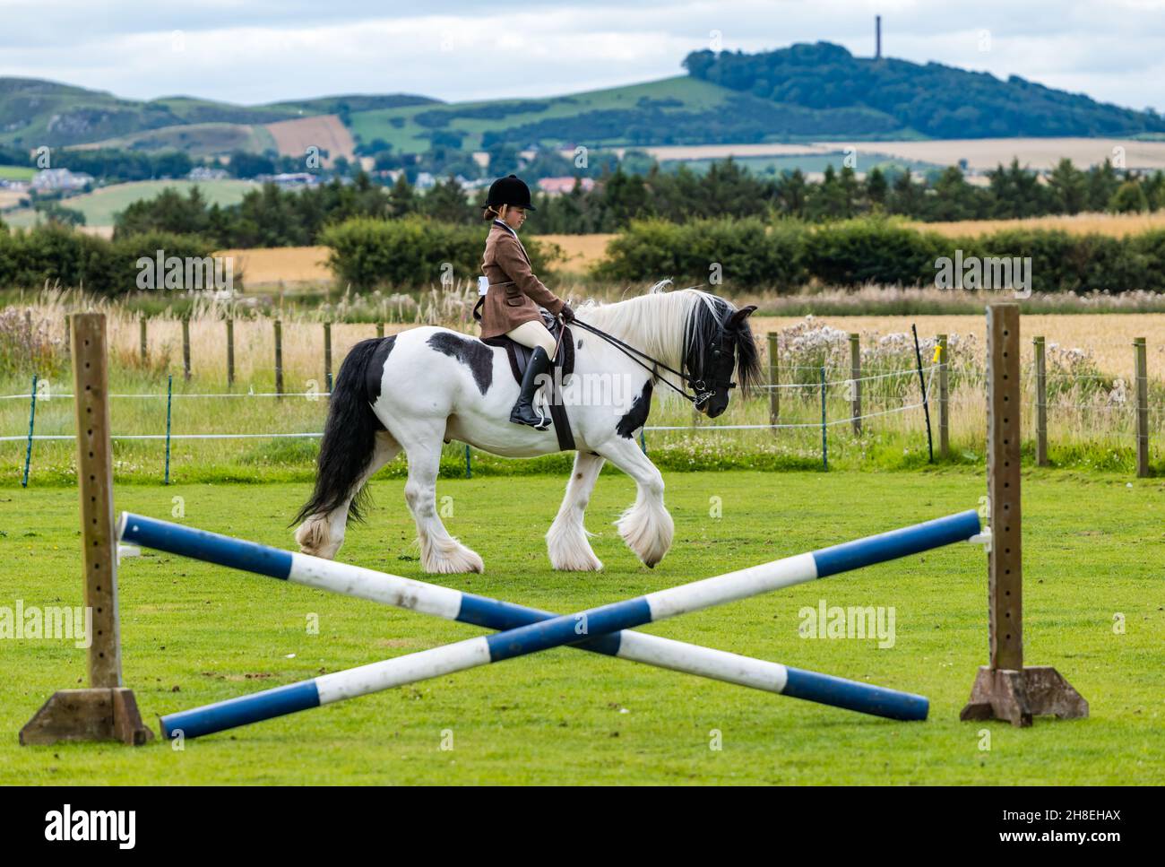 Girl riding horse with hrose jump at outdoor Summer horse event, East Lothian, Scotland, UK Stock Photo