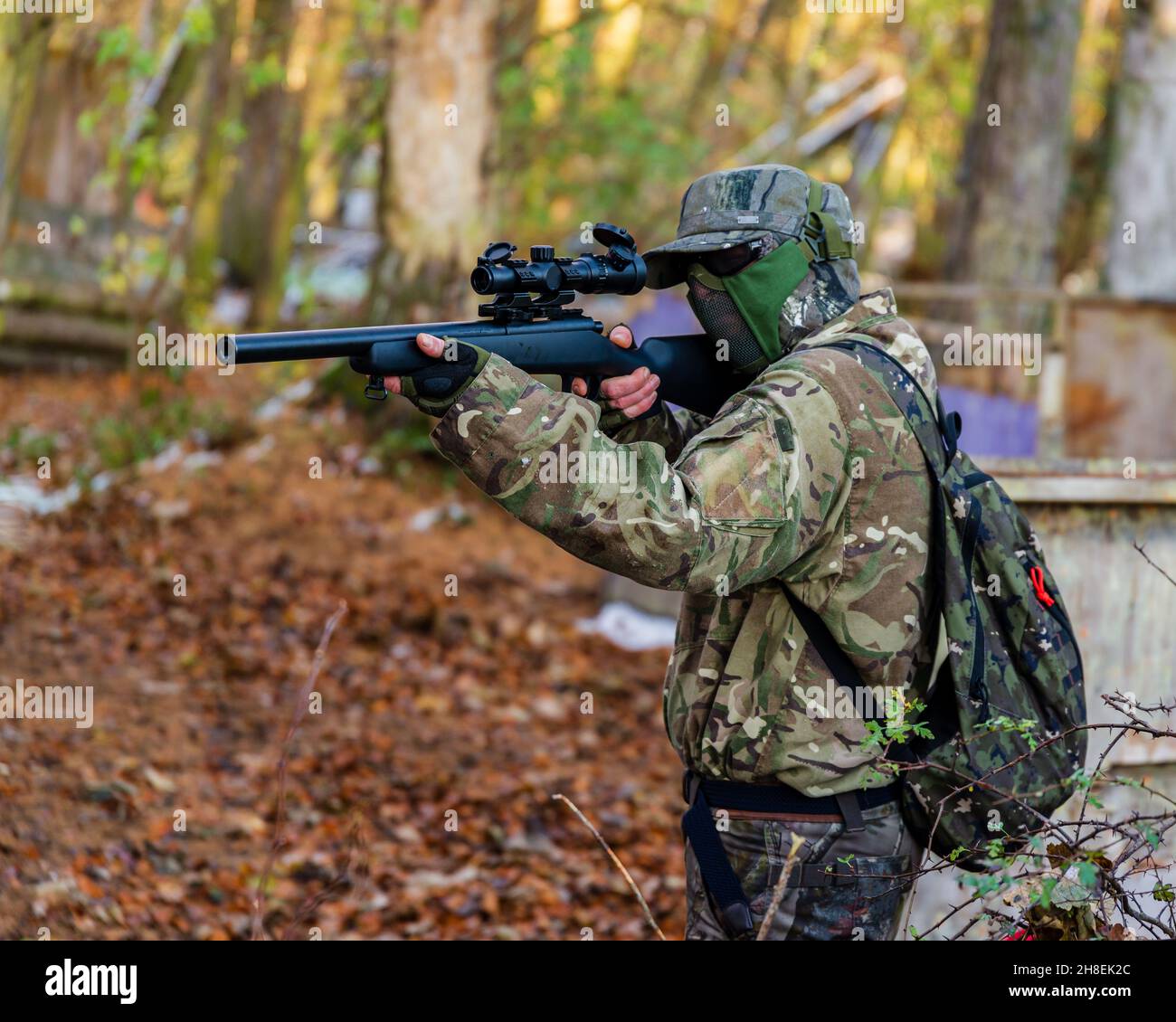 Airsoft man in uniform with sniper rifle, lurking in grass on forest  background. Vertical photo Stock Photo - Alamy