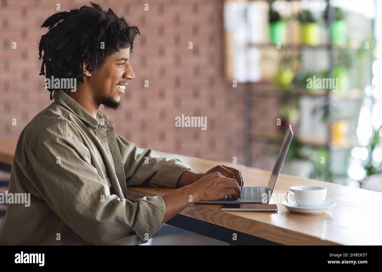 Remote Work. Young African American Freelancer Guy Working With Laptop At Cafe Stock Photo