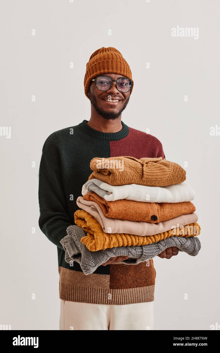 Vertical waist up portrait of young African-American man holding stack of hand knit sweaters and smiling at camera Stock Photo