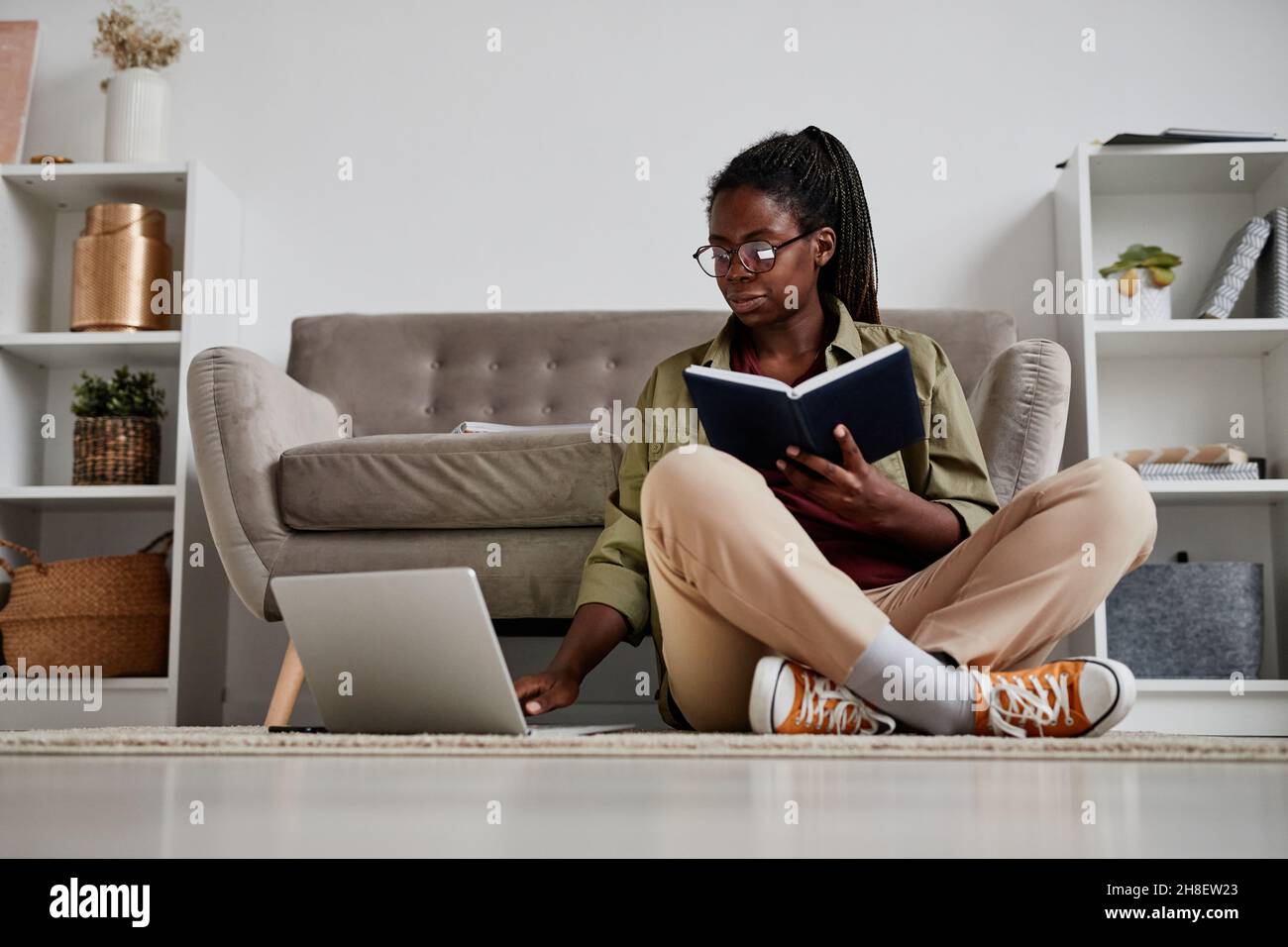 Full length portrait of young African-American woman working from home while sitting on floor in comfortable setting, copy space Stock Photo