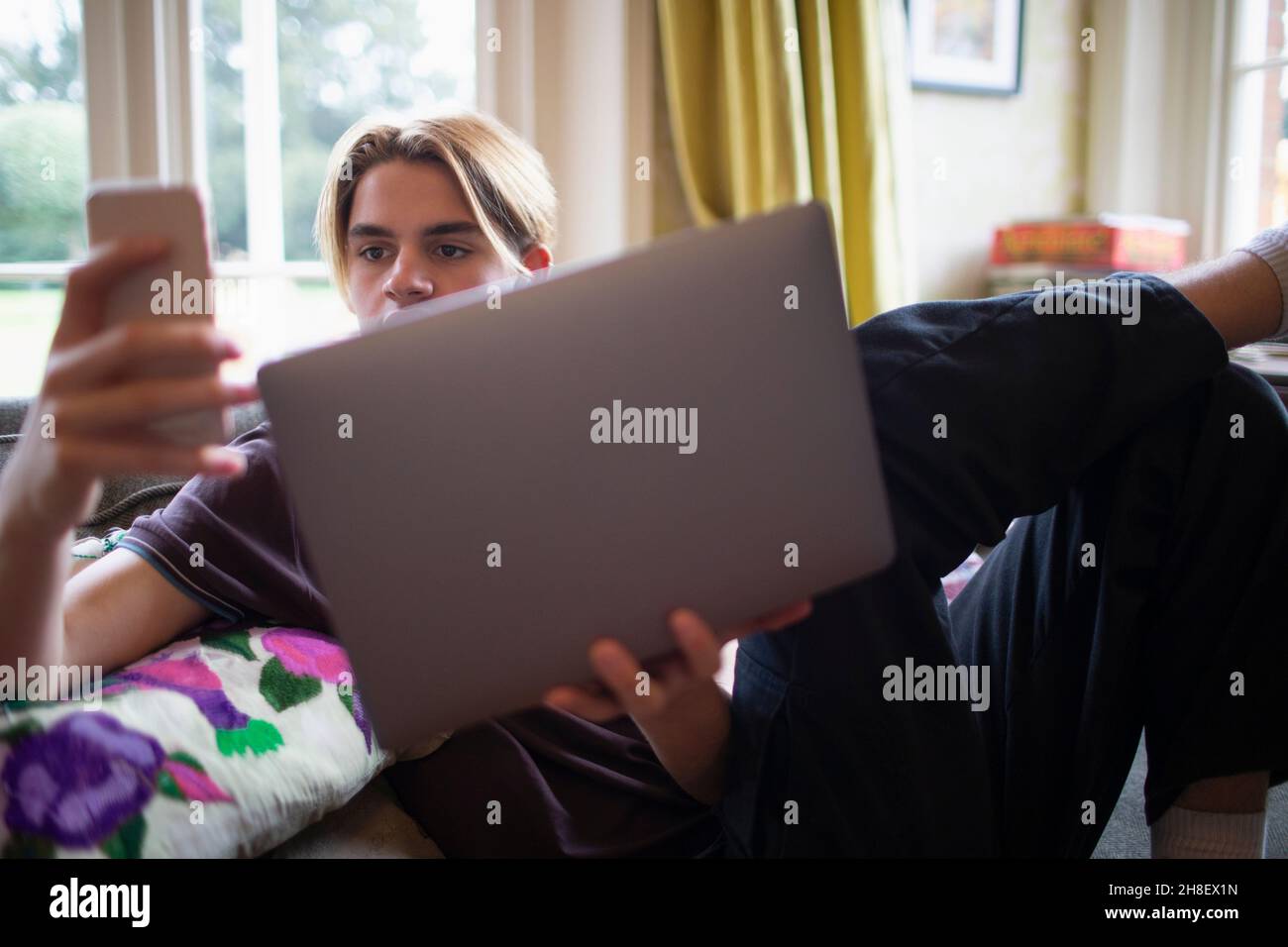 Teenage boy using smart phone and laptop at home Stock Photo - Alamy