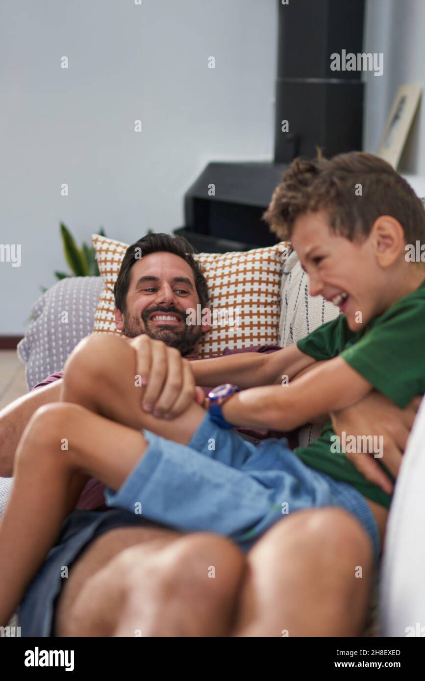 Happy father tickling son on living room sofa Stock Photo