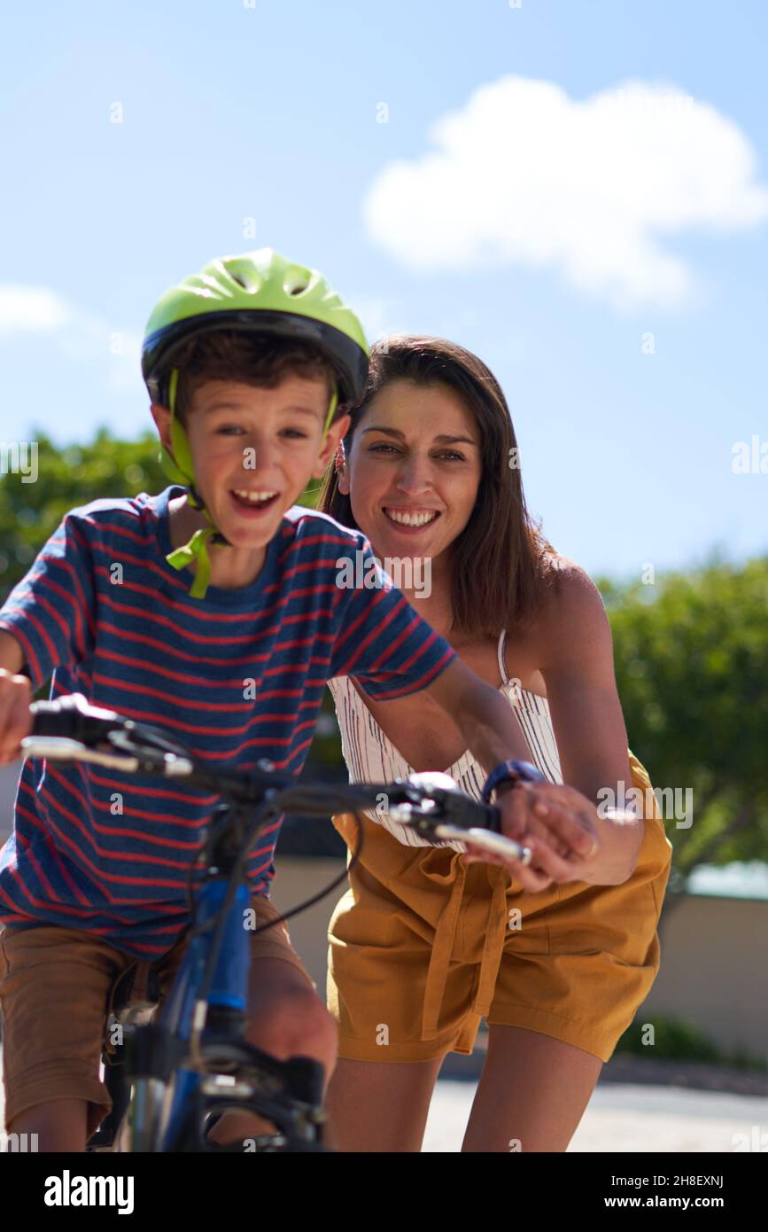 Happy mother helping son ride bike Stock Photo