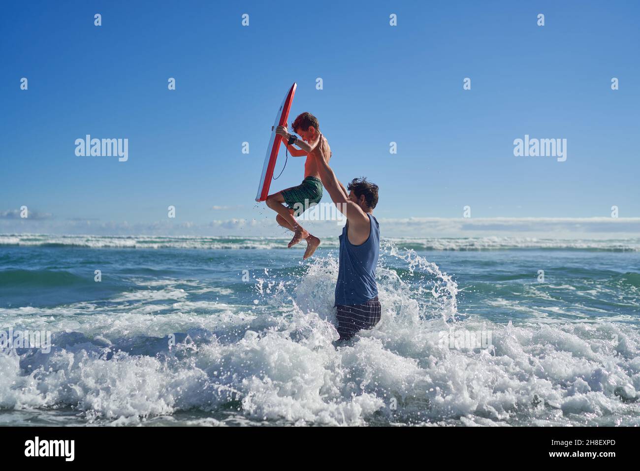 Father lifting son with body board above sunny ocean wave Stock Photo