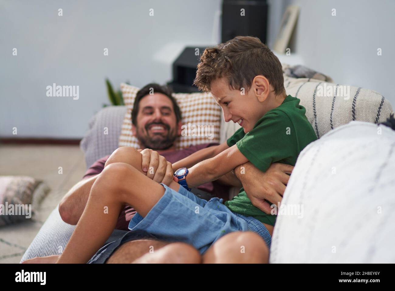 Playful father tickling son on living room sofa Stock Photo