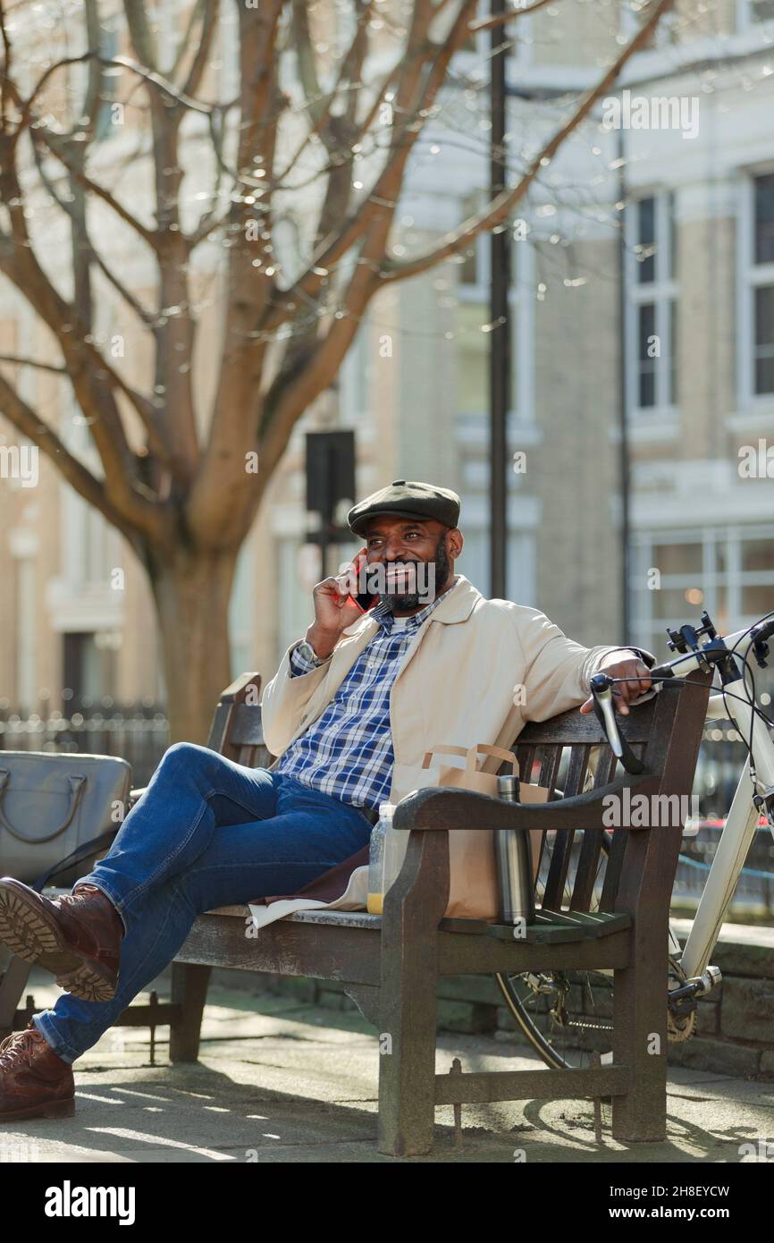 Businessman talking on smart phone on bench in sunny city park Stock Photo