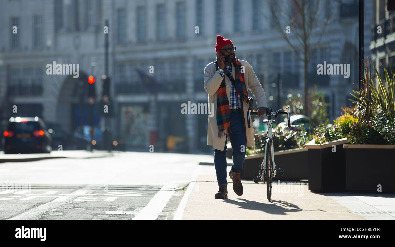 Businessman with bicycle talking on smart phone in sunny city Stock Photo