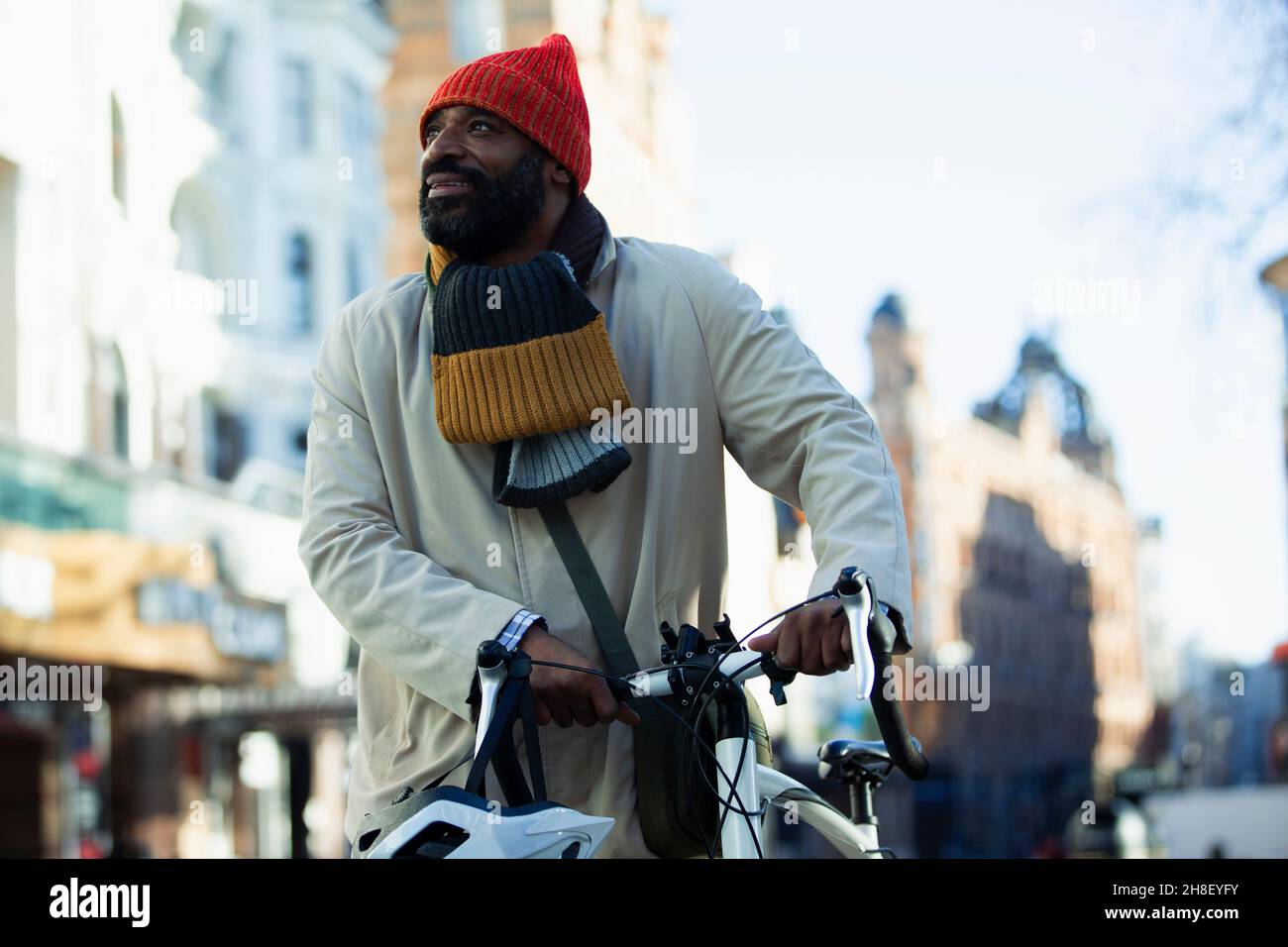 Man in stocking cap and scarf with bicycle on city street Stock Photo