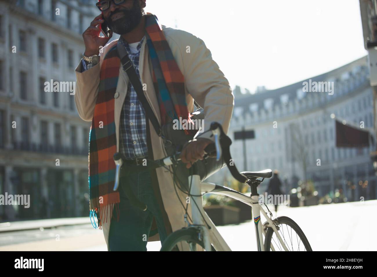 Businessman with bicycle talking on smart phone in sunny city Stock Photo