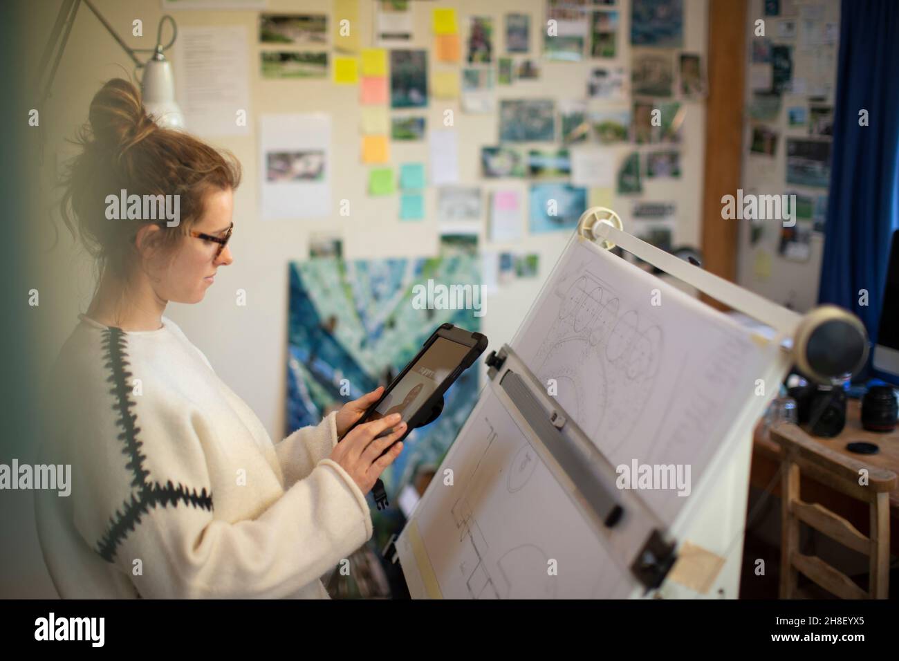 Female architect video chatting at drafting table in home office Stock Photo