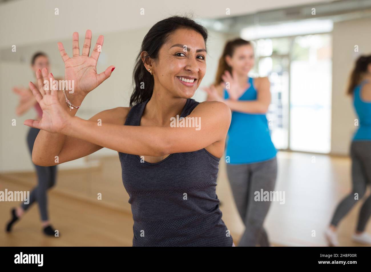 Cheerful hispanic woman practicing vigorous dance in group class Stock Photo