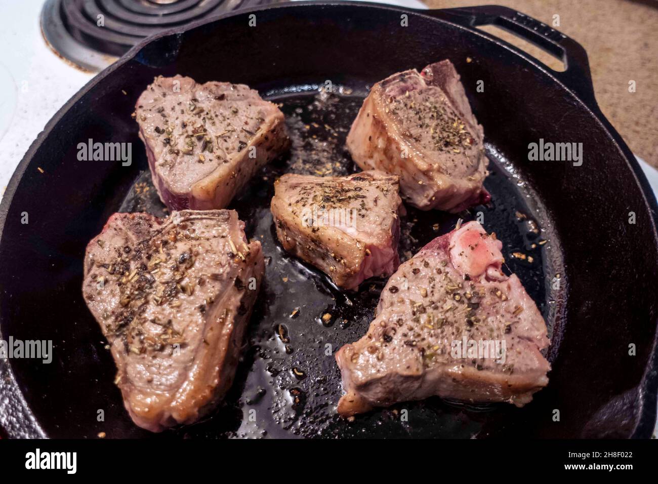 Close up view of several juicy lamb chops sizzling in a hot cast iron