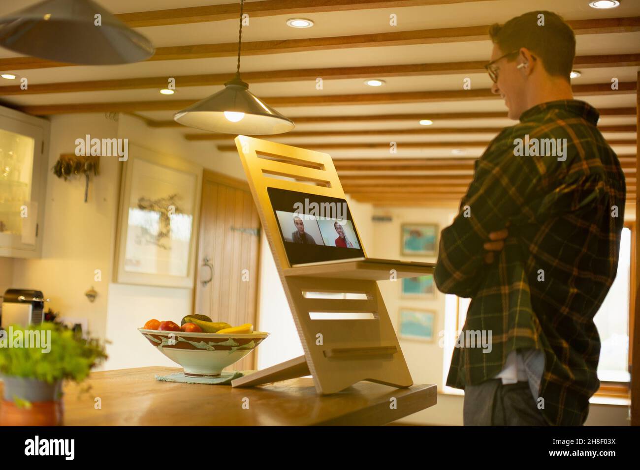 Man video conferencing with colleagues at laptop stand desk in kitchen