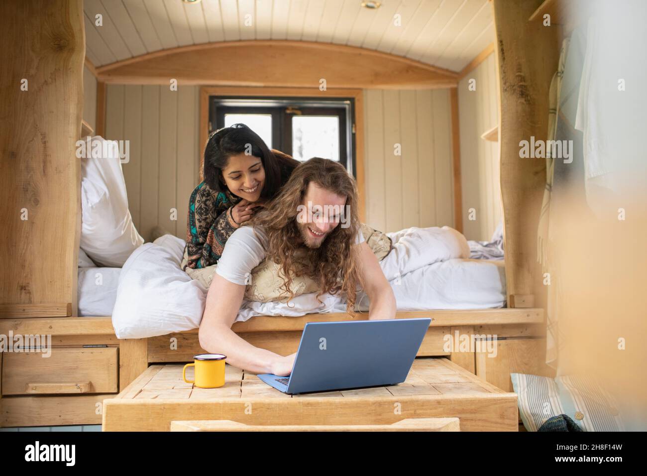 Happy young couple using laptop in tiny cabin bed Stock Photo