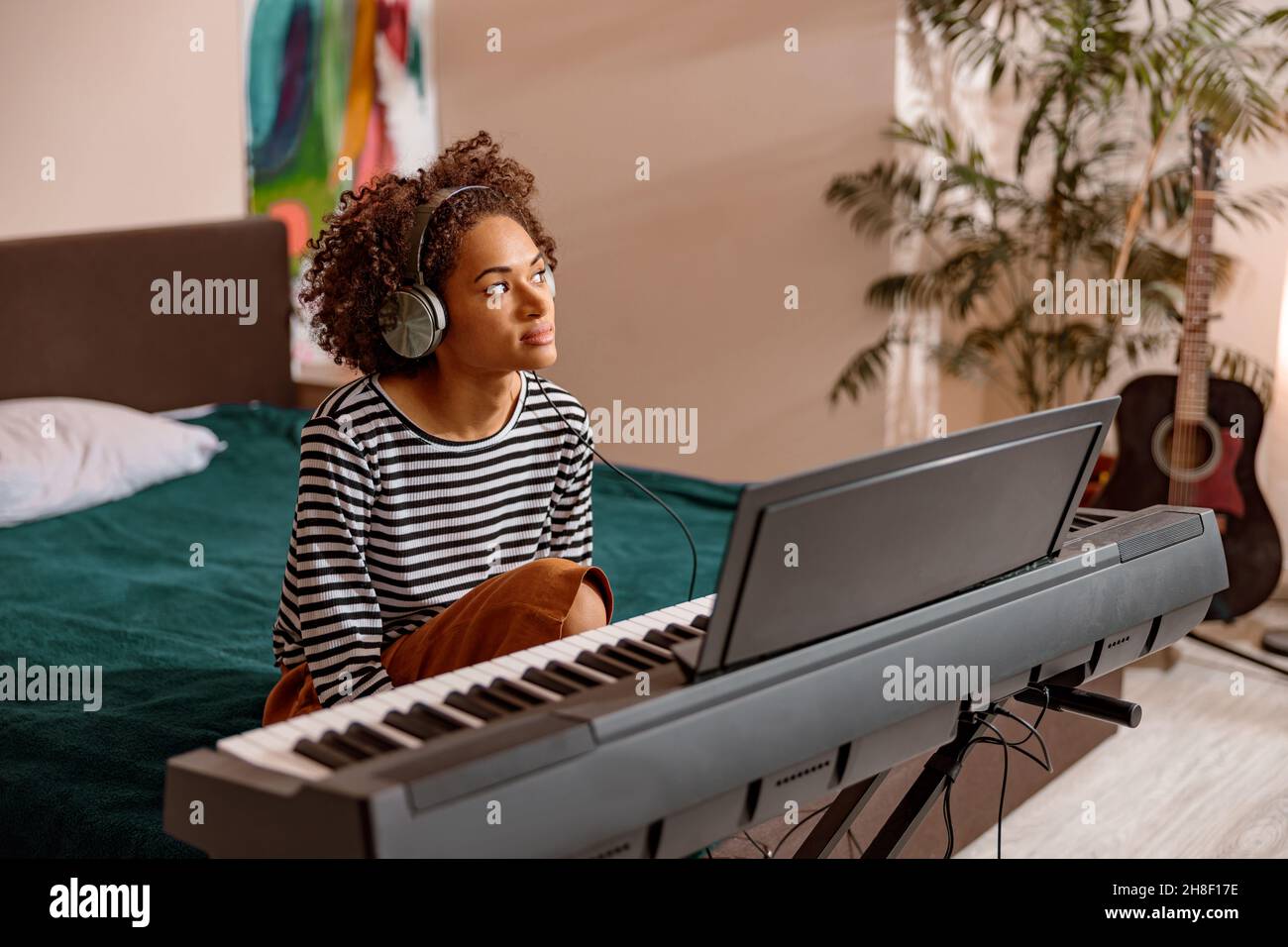 Afro American woman sitting near synthesizer at home Stock Photo