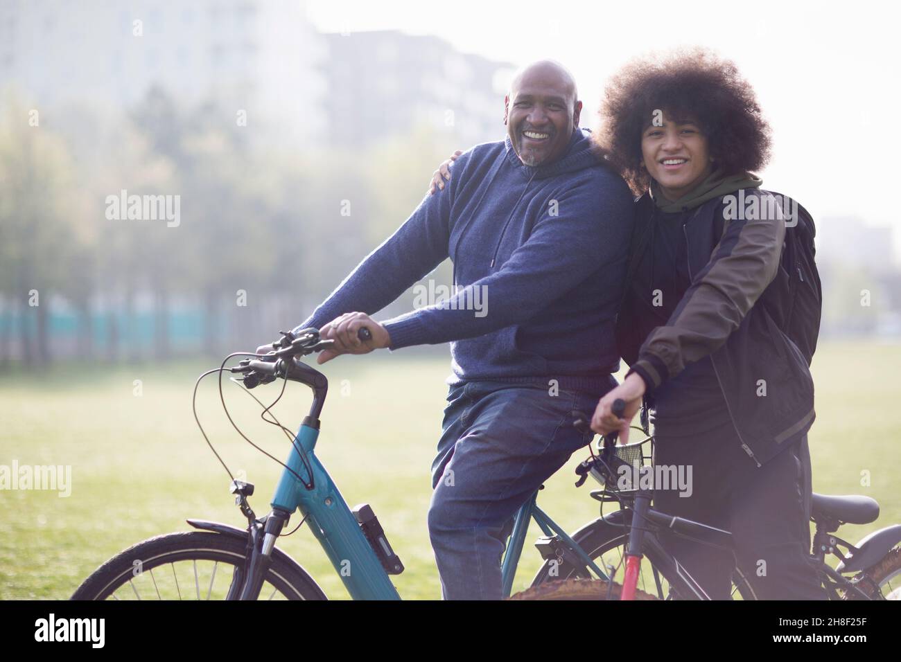 Portrait happy father and teen son on bicycles in urban park Stock Photo