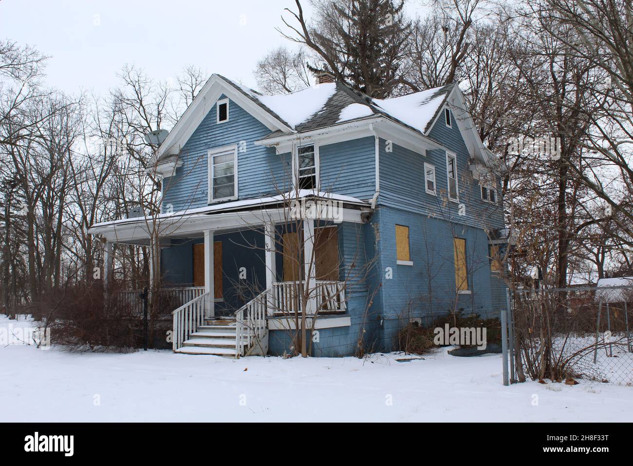 Abandoned and boarded up blue-paneled home in Flint, Michigan in winter Stock Photo