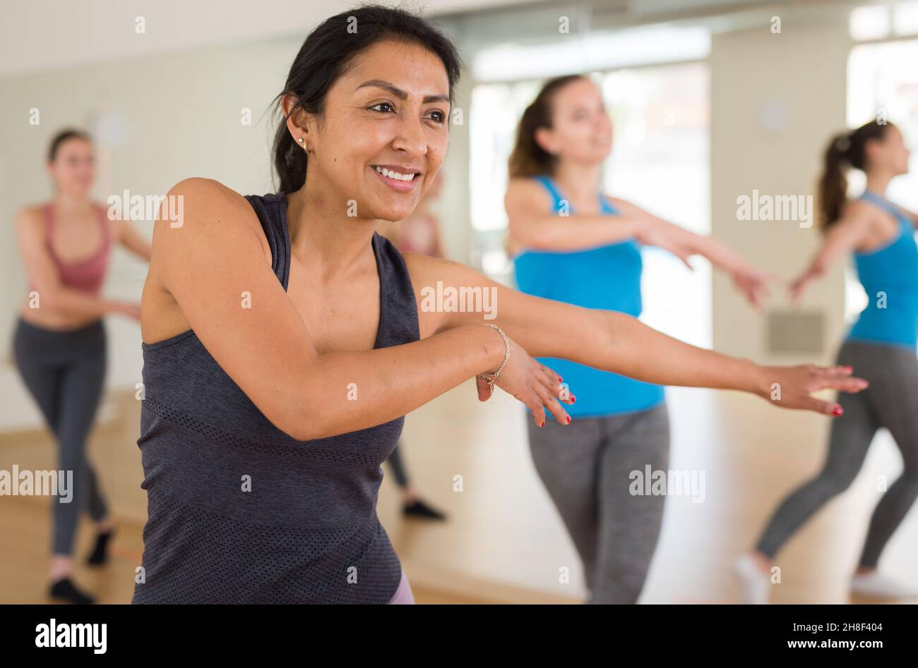 Cheerful hispanic woman practicing vigorous dance in group class Stock Photo