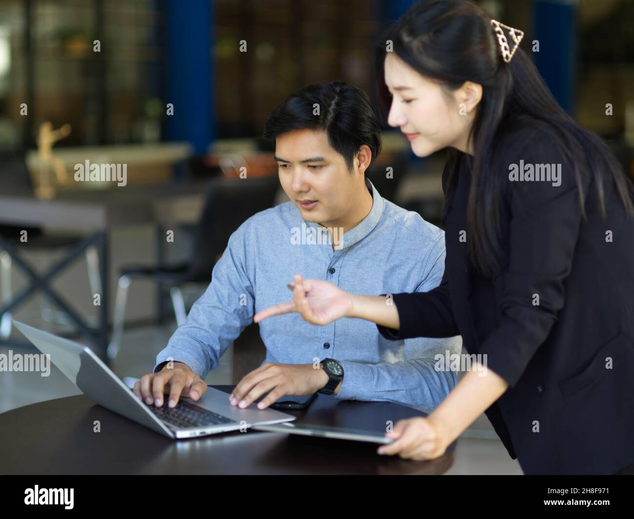 Businessman and businesswoman working together on laptop computer, discussing online project, cooperating in the office. Stock Photo