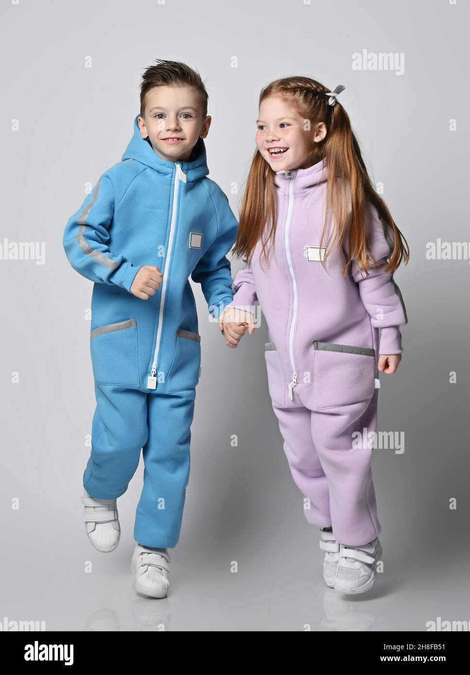 Happy active kids boy and girl in modern blue and pink jumpsuits play and walk together, having fun Stock Photo