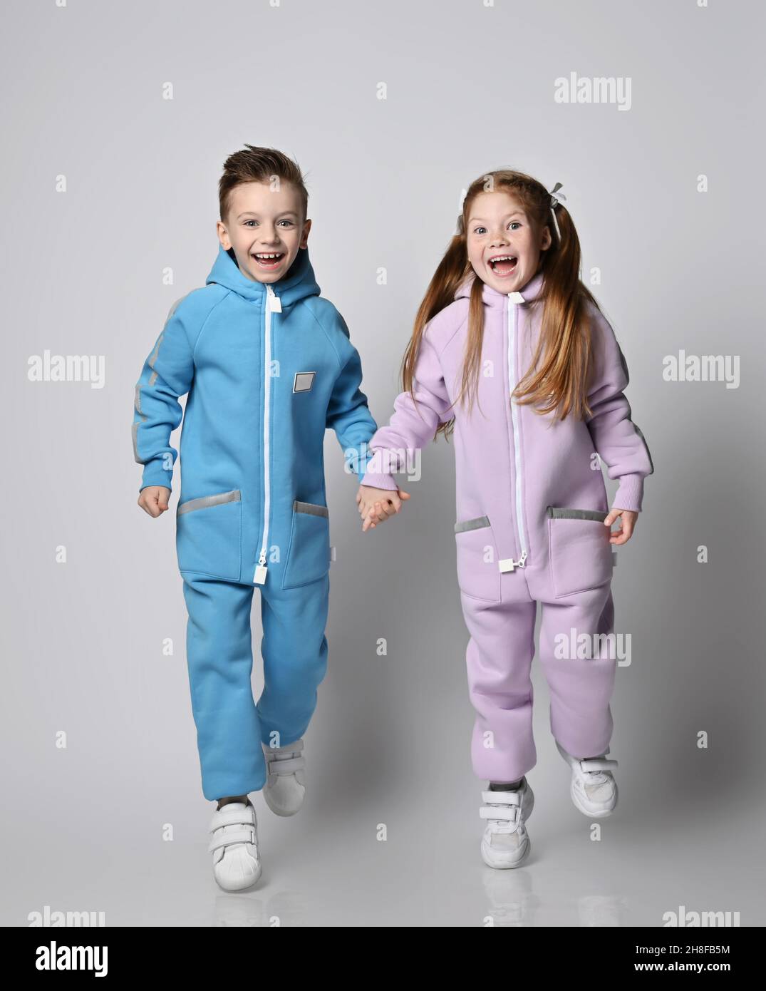 Happy laughing, frolic kids boy and girl in blue and pink jumpsuits with hoods and pockets are running together Stock Photo