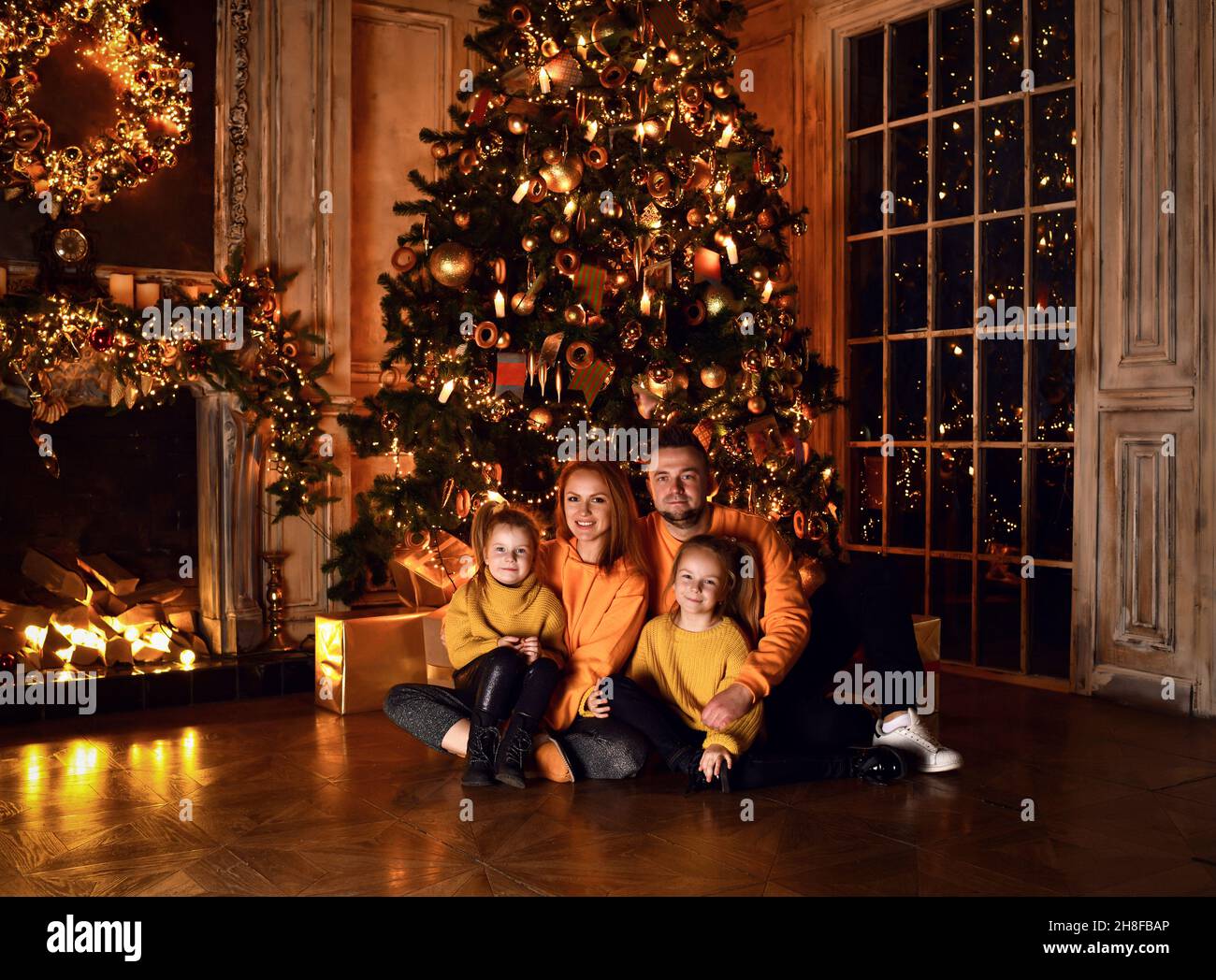 Merry Christmas and Happy Holidays. Mom Father and daughters near decorated the Christmas tree and fireplace Stock Photo