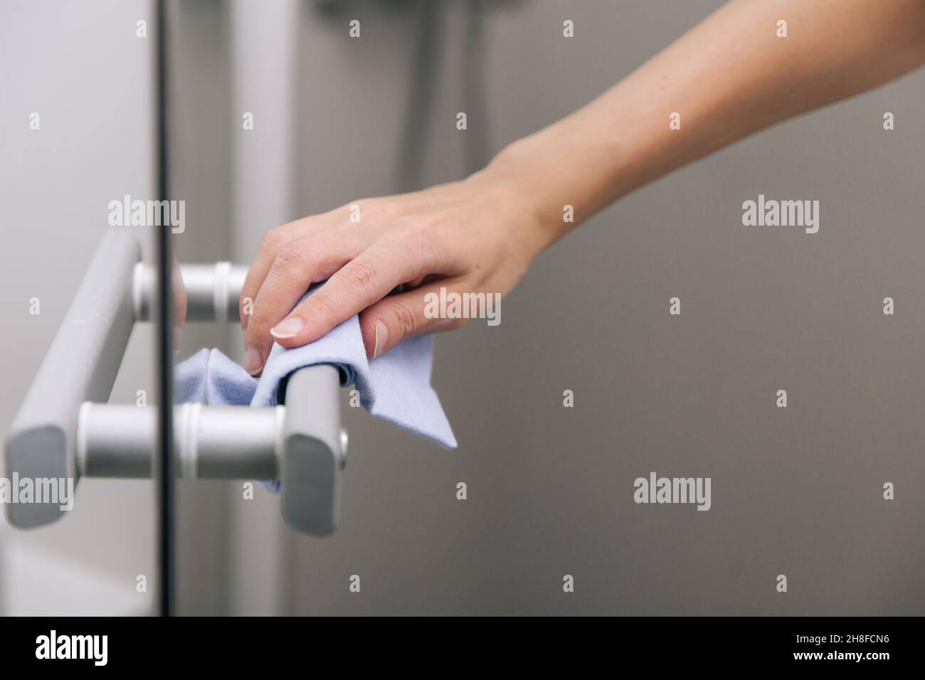 Cleaning glass door handles with an antiseptic wet wipe. Woman hand
