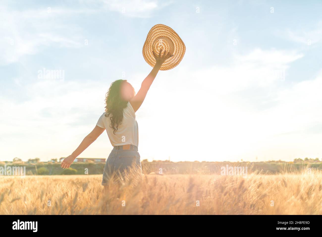 Young woman in a ripe wheat field celebrating with a hat in hand in a sunny wheat field. Concept of prosperity and warmth. Stock Photo