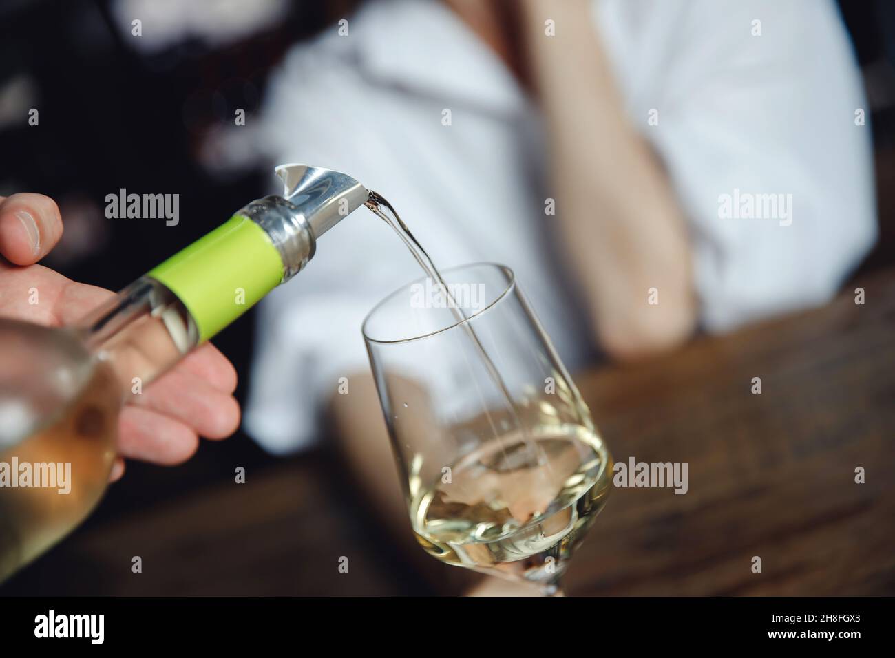 Waiter pouring white wine into glass goblet to young woman. Stock Photo