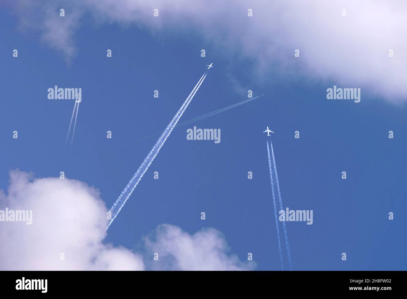 Many distant passenger jet planes flying on high altitude on clear blue sky leaving white smoke trace of contrail behind. Busy air transportation conc Stock Photo