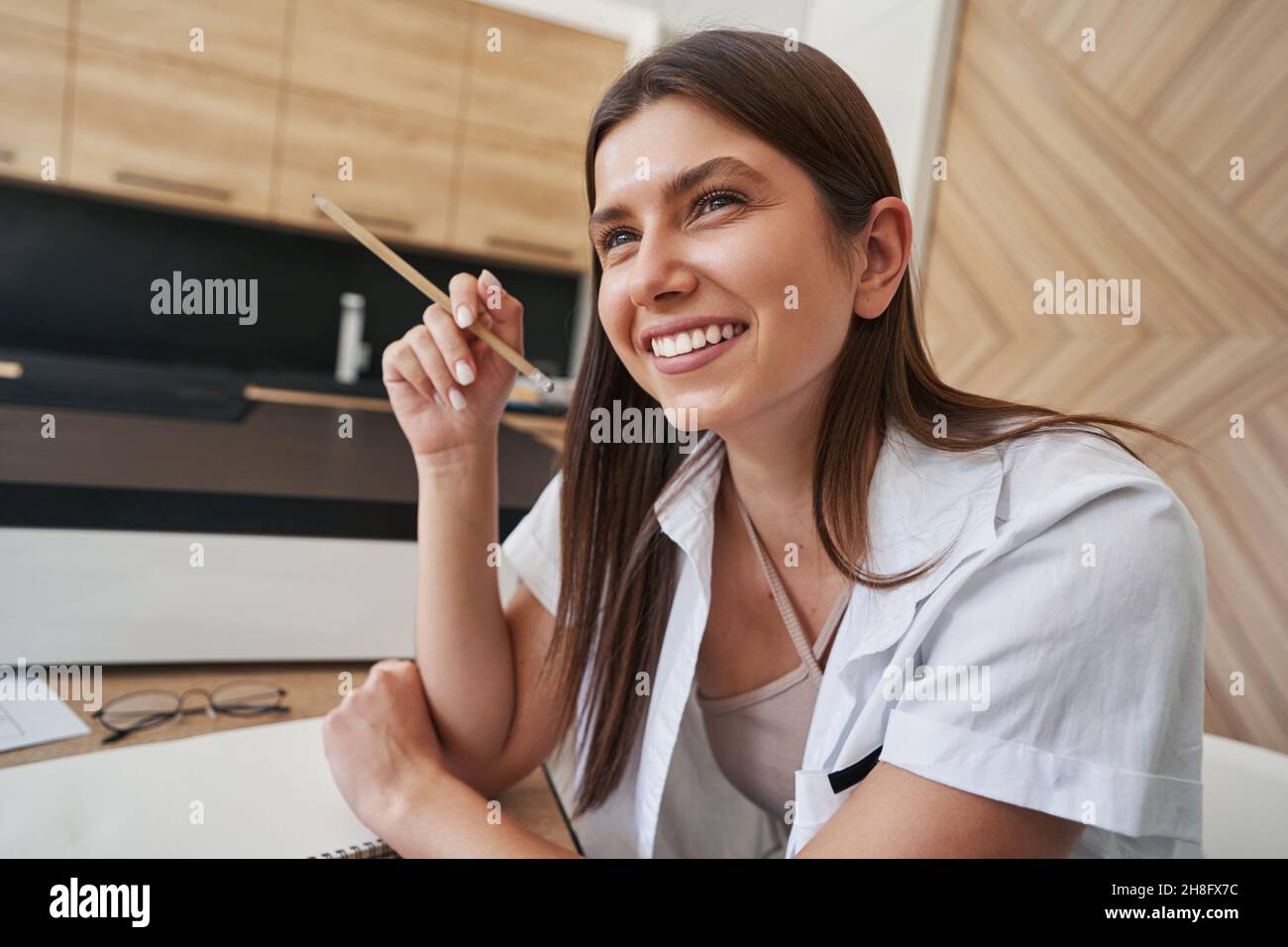 Joyous long-haired lady seated at table in room Stock Photo