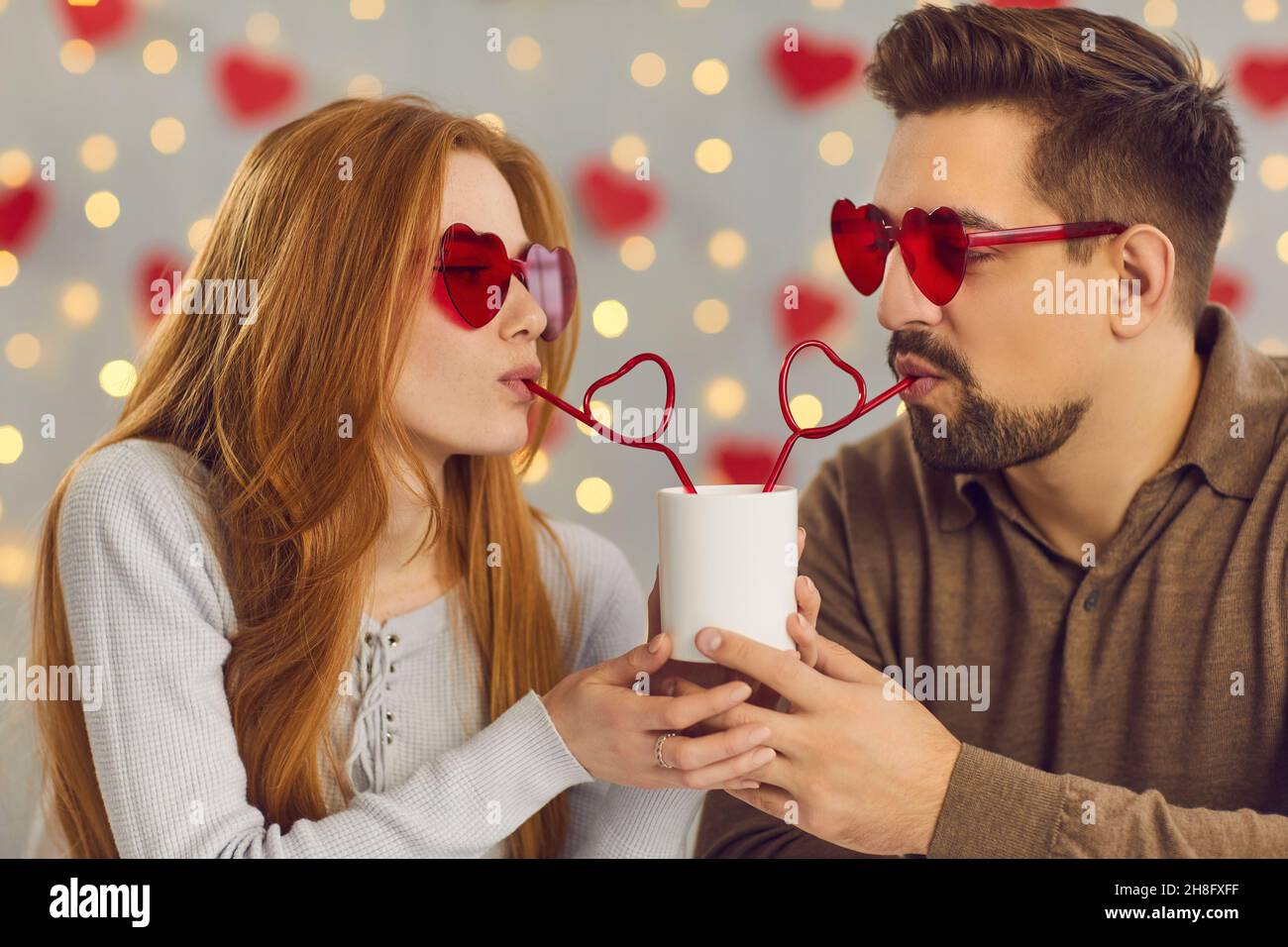Young couple in love celebrating Saint Valentine's Day and sipping drink from one cup Stock Photo