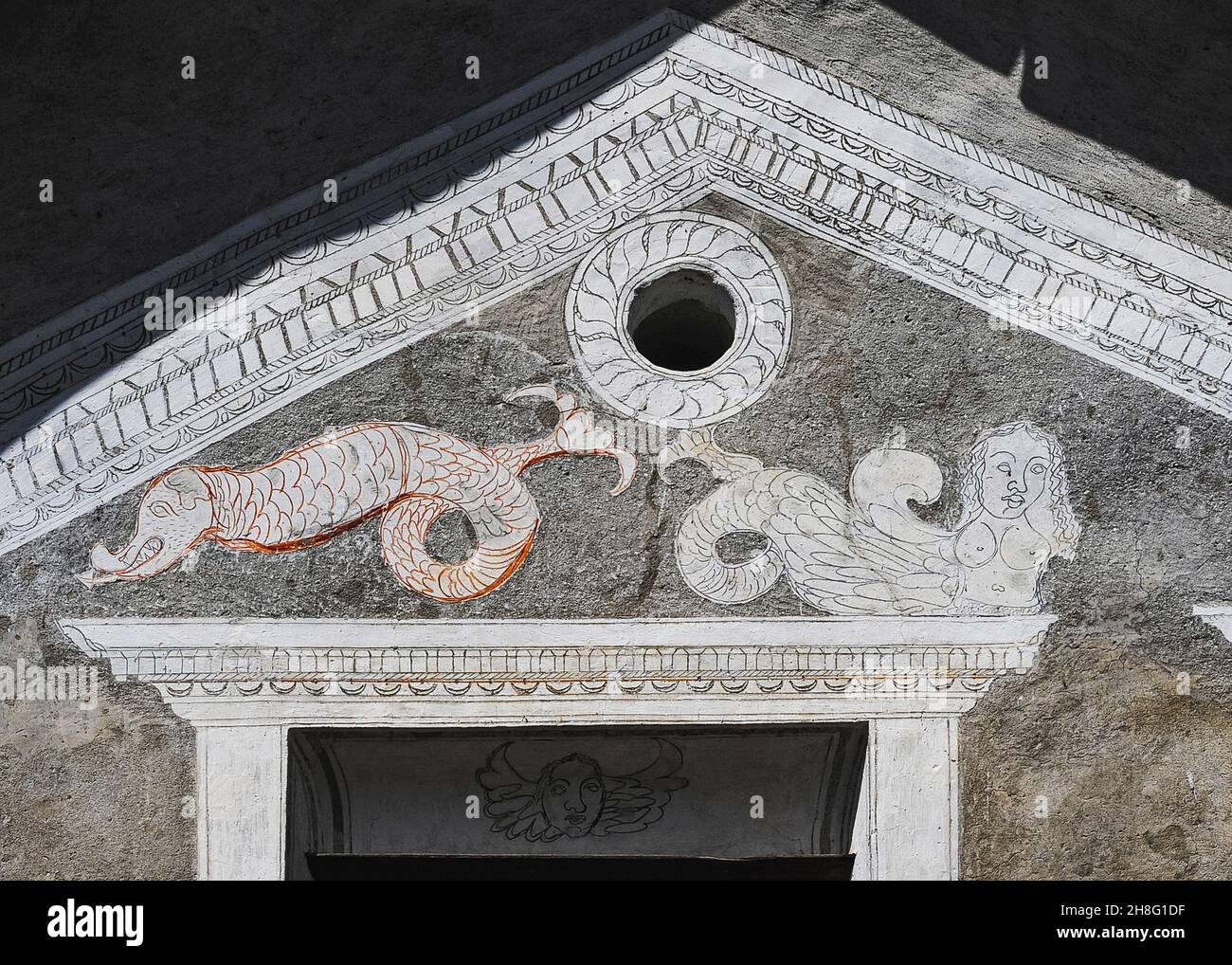 A buxom mermaid reclines beside a scaly sea monster with a forked tail and an arrowhead tongue in eye-catching rustic sgraffito art on the front of a restored traditional family house in Ardez, Graubünden or Grisons canton, eastern Switzerland.  Dragons, mermaids and sea creatures are found on many dwellings in the area restored by local sgraffito artists in the early 1900s. Stock Photo
