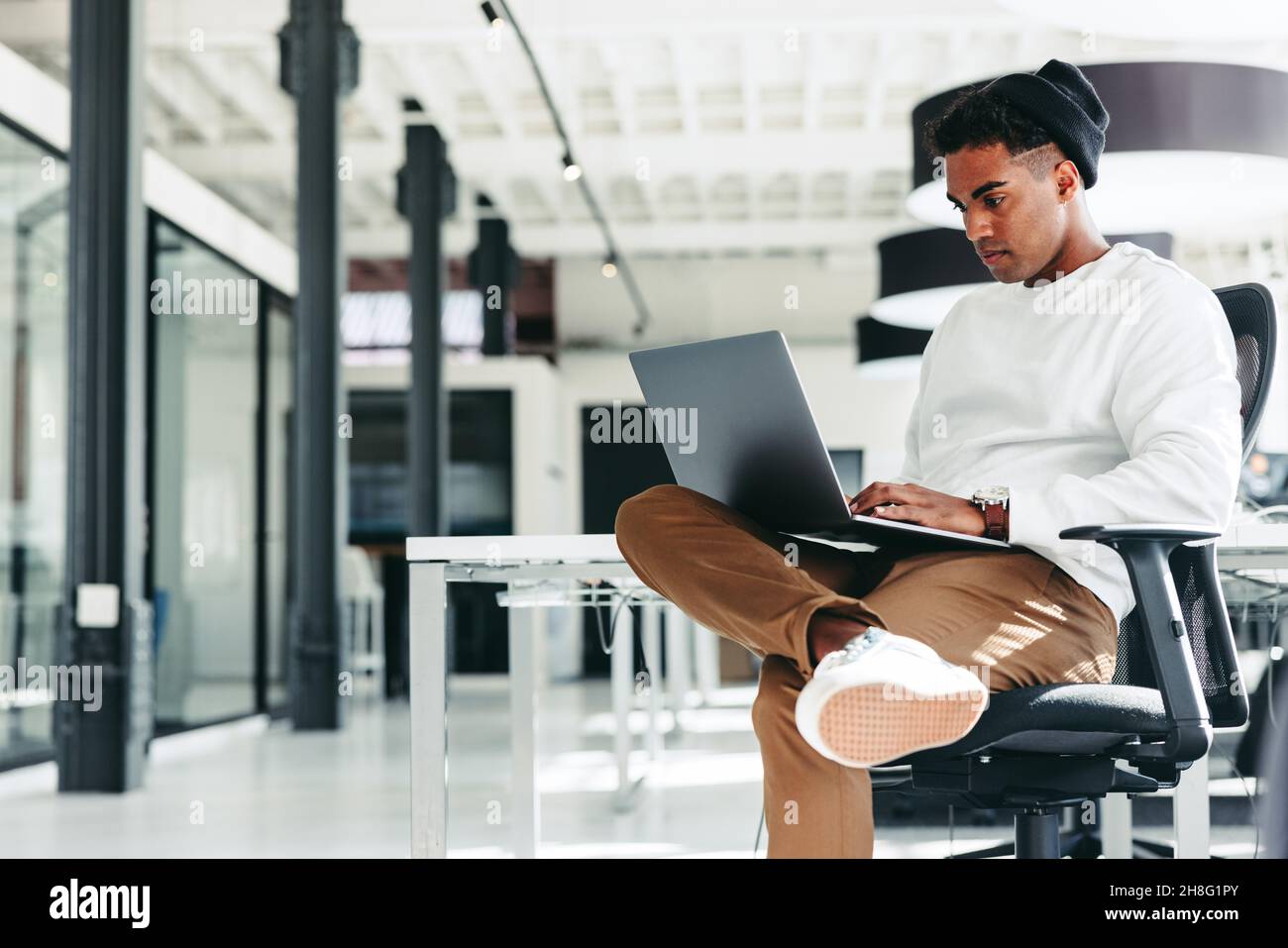 Focused software developer working on a new project. Young businessman using a laptop while sitting in a modern workplace. Creative businessman workin Stock Photo