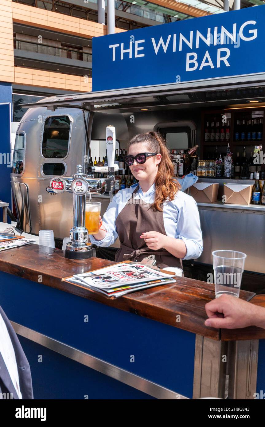 The Winning Post Bar at Royal Ascot racecourse, Berkshire, UK. Barmaid serving a customer with a draught pint of lager. Serving alcohol on sunny day Stock Photo