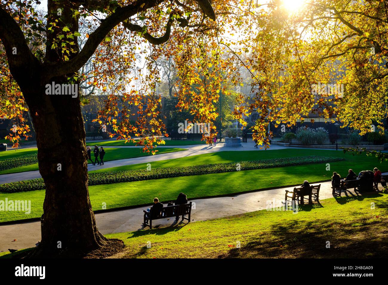 People sit on benches in Victoria Embankment Gardens Stock Photo