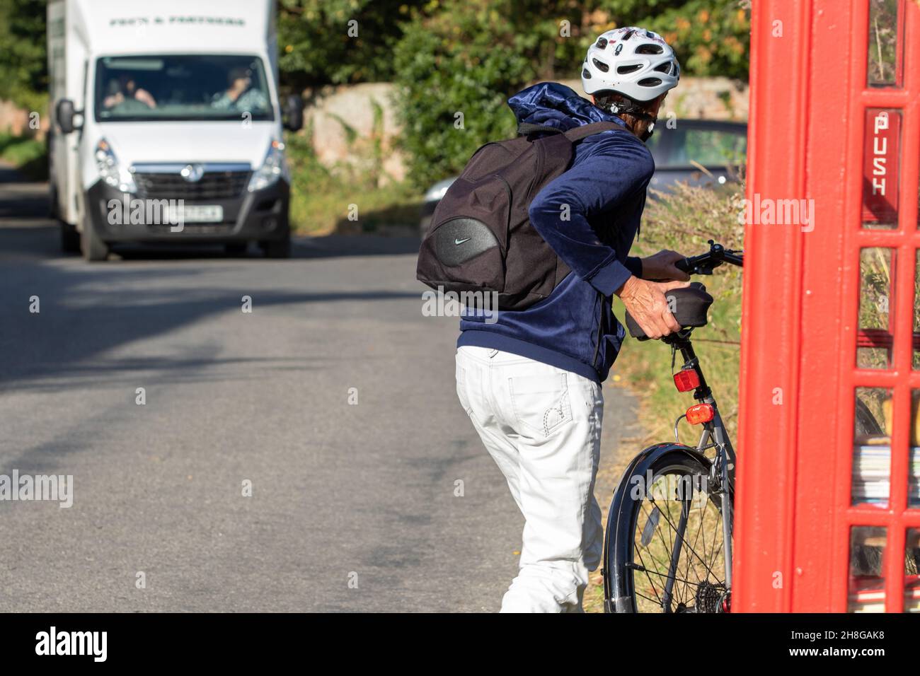 Dismounted woman cyclist parks her bike near a red telephone box Stock Photo