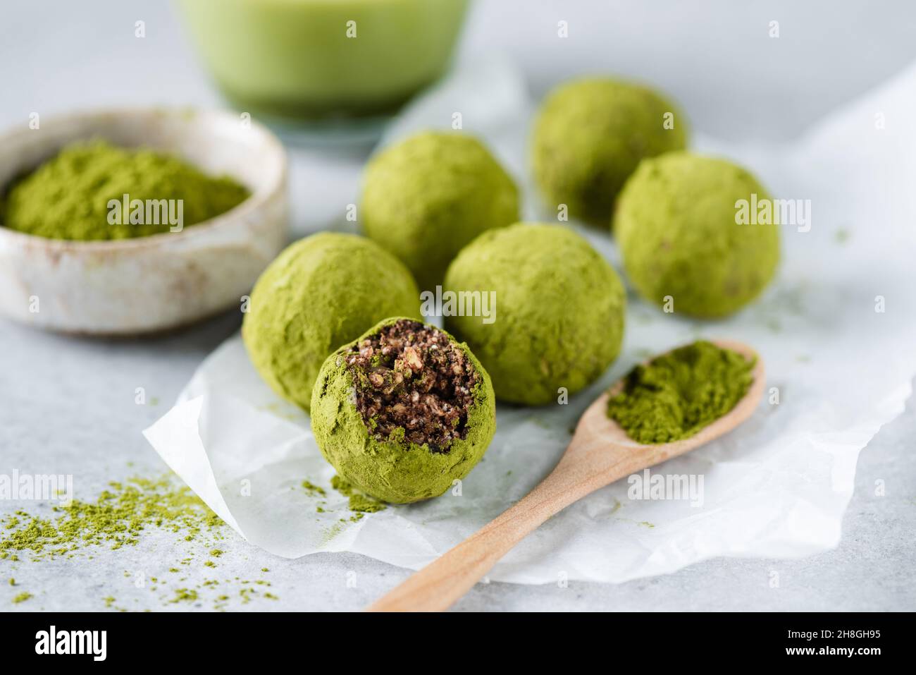 Raw matcha green tea energy balls with dates and nuts on parchment paper, candy missing a bite