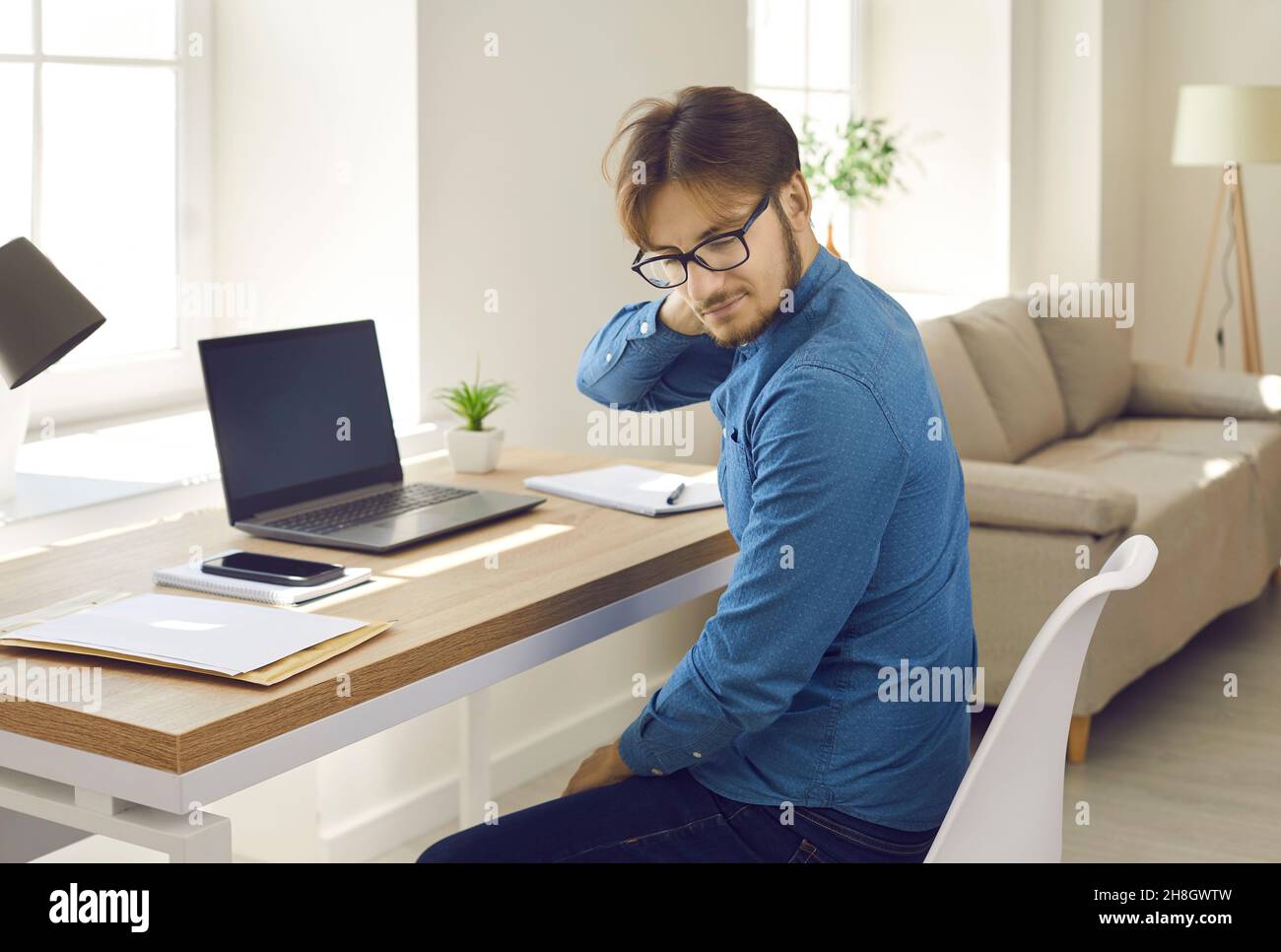Tired man who has neck pain sitting at his desk and working on his laptop computer Stock Photo