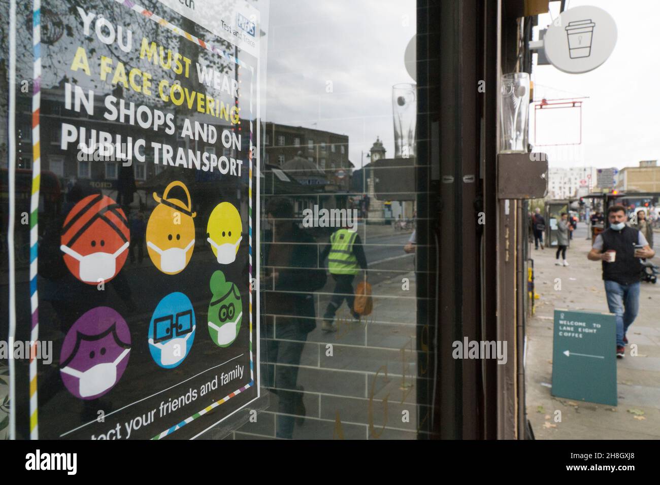 London, UK, 30 November 2021: In Clapham shoppers are now obliged by law to wear a face mask in shops or on public transport. In a shop window a colourful sign depicting a diverse array of people wearing face masks, supplied by Lambeth Council, reminds people of the change in regulations which has come into effect today. Anna Watson/Alamy Live News Stock Photo
