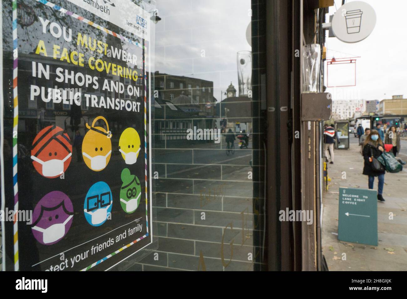 London, UK, 30 November 2021: In Clapham shoppers are now obliged by law to wear a face mask in shops or on public transport. In a shop window a colourful sign depicting a diverse array of people wearing face masks, supplied by Lambeth Council, reminds people of the change in regulations which has come into effect today. Anna Watson/Alamy Live News Stock Photo