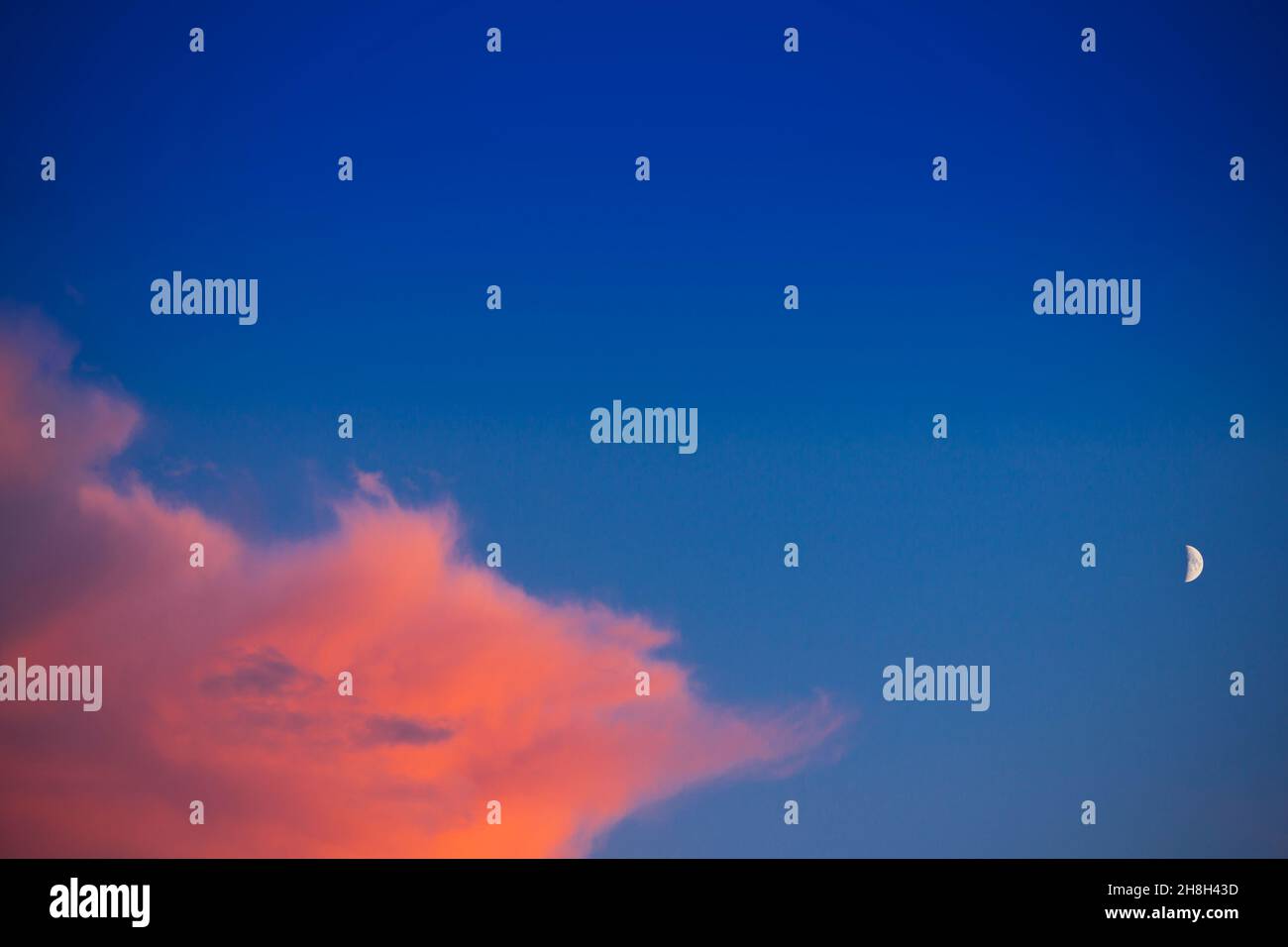 Colorful orange cloud against blue sky with a half moon at sunset, lots of copy space. Stock Photo