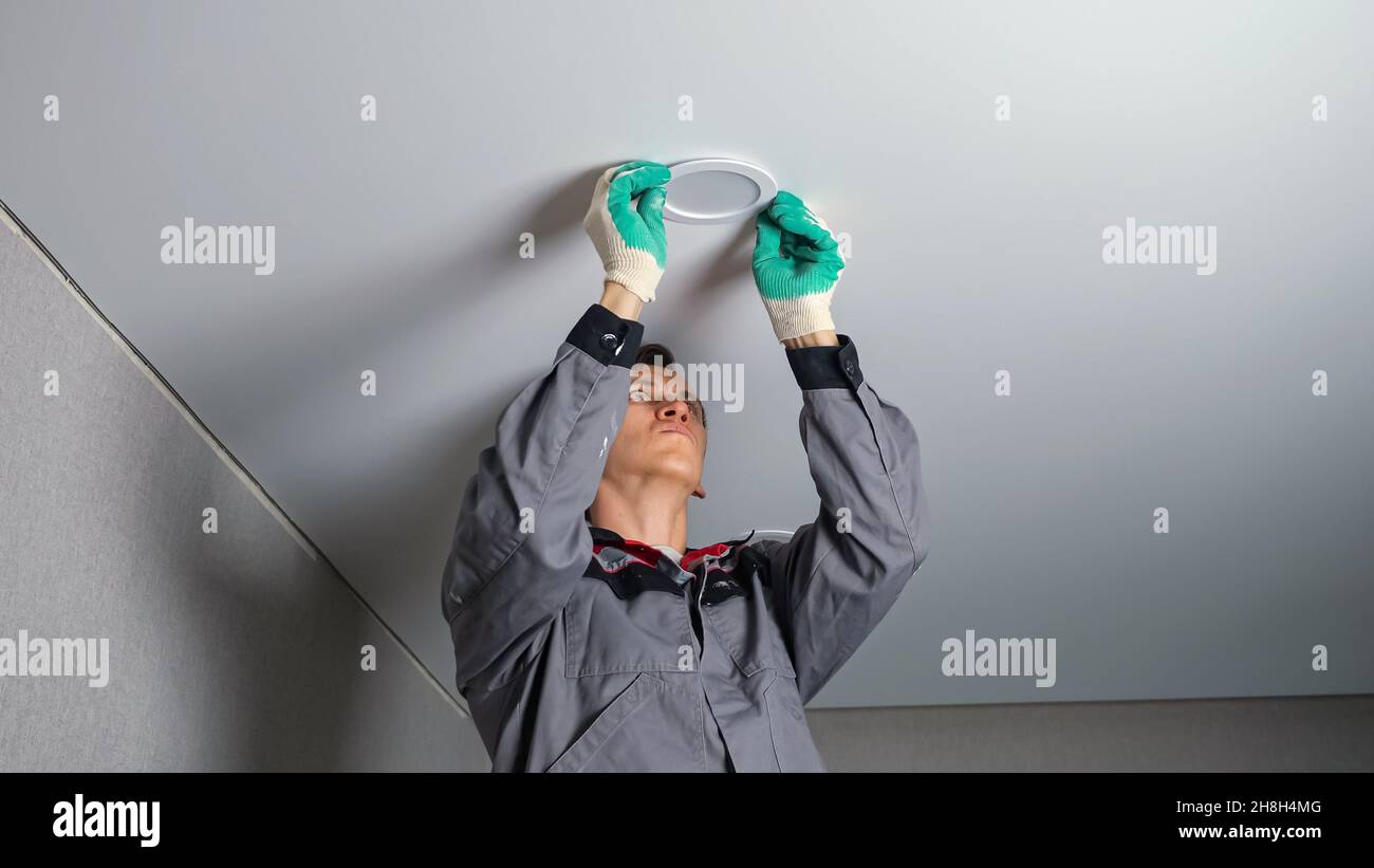 Electrician installs light on ceiling at flat renovation Stock Photo